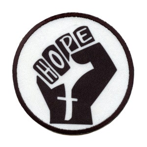 Może przedstawiać: Biała okrągła łatka z uniesioną czarną pięścią i napisem "HOPE" napisanym białymi literami na pięści.