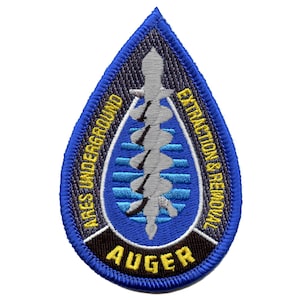 Op de afbeelding: Een blauwe, druppelvormige patch met de woorden "NARES UNDERGROUND EXTRACTION & REMOVAL" en "AUGER" in gele tekst. De patch heeft een grijs en blauw ontwerp in het midden.