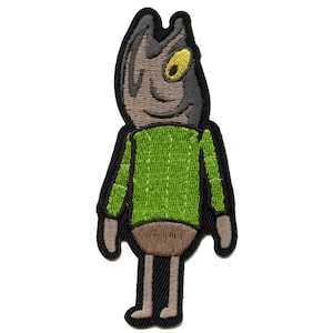 Könnte beinhalten: Gestickter Aufnäher eines Cartoon-Fischs, der einen grünen Pullover trägt. Der Fisch hat einen braunen Körper, schwarze Augen und ein gelbes Auge.