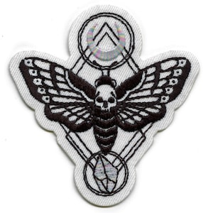 May include: Black and white embroidered patch featuring a moth with a skull head, surrounded by geometric shapes and a crescent moon with iridescent thread.