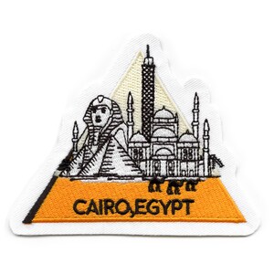 May include: An embroidered patch with a white background and a yellow triangle. The triangle features a black and white illustration of the Sphinx, the Great Pyramid, and a mosque. The text "CAIRO, EGYPT" is printed in black on the yellow triangle.