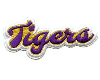 Op de afbeelding: Paarse en gouden geborduurde strijk-op patch met het woord "Tigers" in een cursief schrift.