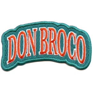 Può includere: Una toppa ricamata di colore blu turchese con il testo "DON BROCO" in lettere bianche e arancioni.