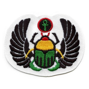 May include: An embroidered patch featuring a scarab beetle with wings, a red circle with an ankh symbol, and green, yellow, and black colors.