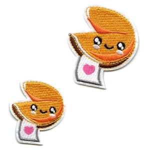 May include: Two embroidered iron-on patches of fortune cookies with smiling faces and a pink heart on a white background.