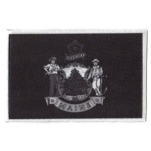 May include: Black and white embroidered patch featuring the state seal of Maine. The seal depicts a pine tree, a farmer, and a sailor, with the words "DIRIGO" and "MAINE" around the design.