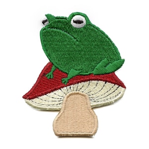 May include: Green frog sitting on a red and white mushroom. The mushroom has a white top with brown gills and a tan stem.