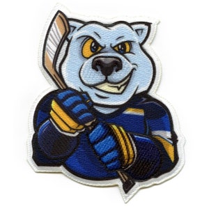 Puede incluir: Una mascota de hockey azul y blanca con una expresión feroz, sosteniendo un palo de hockey. La mascota es un oso con un uniforme de hockey amarillo y negro.