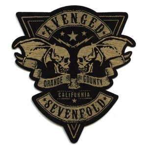 Könnte beinhalten: Schwarzer und goldener gestickter Patch in Dreiecksform mit dem Text "Avenged Sevenfold". Der Patch zeigt zwei Schädel mit Flügeln und den Text "Orange County California".