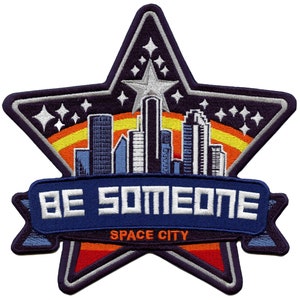 May include: Embroidered patch featuring a blue star shape with a cityscape inside. The star has a yellow and orange sunset behind it. The text "BE SOMEONE SPACE CITY" is on a blue banner below the star.