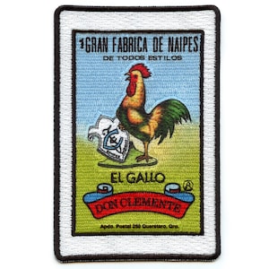 May include: A white and black embroidered patch featuring a rooster holding a shield with the text "El Gallo Don Clemente" and the text "1 Gran Fabrica de Naipes De Todos Estilos" at the top.