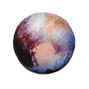 May include: A round, embroidered patch depicting a colourful image of Pluto, a dwarf planet in our solar system. The patch is a dark blue colour with a light blue, pink, and orange swirl pattern.