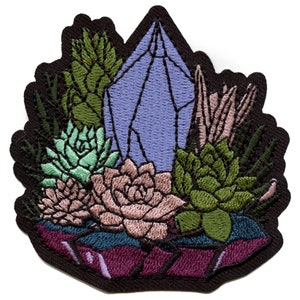 May include: An embroidered patch featuring a purple crystal surrounded by green and pink succulents. The crystal is surrounded by a dark purple border.