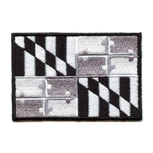 Puede incluir: Un parche bordado en blanco y negro con la bandera del estado de Maryland. La bandera es un diseño a cuadros blanco y negro con una cruz amarilla y roja en el centro.