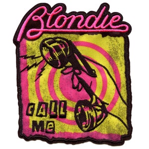 Könnte beinhalten: Ein schwarzer und gelber gestickter Aufnäher mit dem Text "Blondie" in rosa Schrift und einer schwarzen Silhouette eines Wählscheibentelefons mit dem Text "Call Me" darunter.