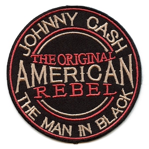 May include: A black embroidered patch with the text "Johnny Cash The Original American Rebel The Man In Black" in tan and red lettering.