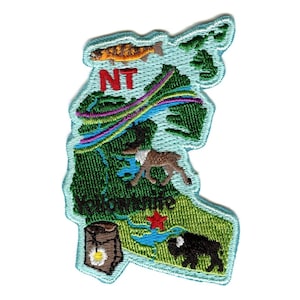 May include: An embroidered patch depicting the outline of the Northern Territory of Australia. The patch is light blue with green and brown details. It features a fish, a deer, a bison, a tree stump, and the text "NT" and "Northern Territory".