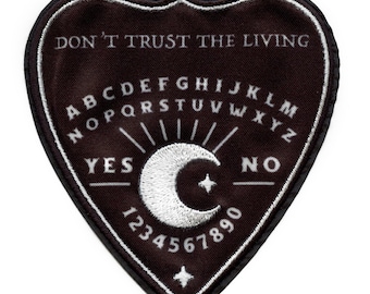 May include: A black heart-shaped patch with white stitching. The patch features a Ouija board design with the letters A-Z, numbers 1-9, and the words "YES" and "NO". The text "DON'T TRUST THE LIVING" is printed at the top of the patch.