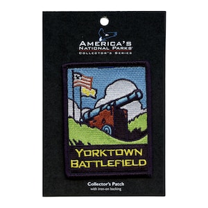 Op de afbeelding: Een geborduurde patch in blauw, groen en geel met een kanon en een Amerikaanse vlag. De tekst "Yorktown Battlefield" staat op de patch. Het maakt deel uit van de "America's National Parks Collector's Series".