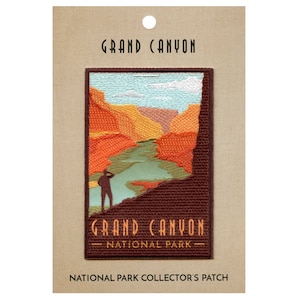 May include: An embroidered patch featuring a scenic view of the Grand Canyon National Park. The patch depicts a person standing on a cliff overlooking the canyon, with a river winding through the red rock formations. The text "Grand Canyon National Park" is embroidered below the image.