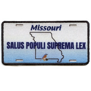 May include: Embroidered patch resembling a Missouri license plate. The patch features the state name, outline, and the motto "SALUS POPULI SUPREMA LEX" in blue text. A small bird graphic is also included.