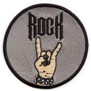 May include: A round gray embroidered patch with black stitching. The patch features a black embroidered word "ROCK" and a black embroidered hand making the rock and roll hand gesture.