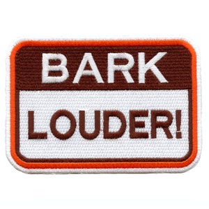 May include: Embroidered patch with the words "BARK LOUDER!" in white and brown lettering. The patch has a brown top border, a white center, and an orange and brown border. The patch is rectangular with rounded corners.