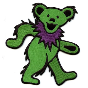 Könnte beinhalten: Grün-violetter gestickter Aufnäher mit einem Cartoon-Bären mit einem breiten Grinsen. Der Bär geht und trägt ein violettes Halsband mit gezacktem Rand.