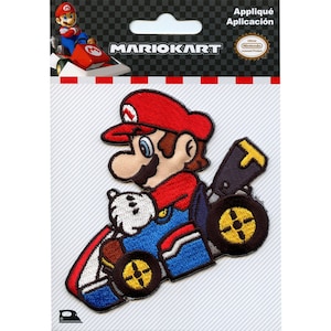 May include: An iron-on patch featuring Mario from the Mario Kart video game series. Mario is depicted in his signature red and blue overalls, driving a kart with a yellow steering wheel. The patch is officially licensed by Nintendo.