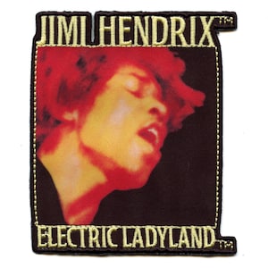 Könnte beinhalten: Ein braunes und golden besticktes Patch mit dem Text "Jimi Hendrix" und "Electric Ladyland" in gelber Schrift. Das Patch zeigt ein Nahaufnahmebild von Jimi Hendrix' Gesicht.