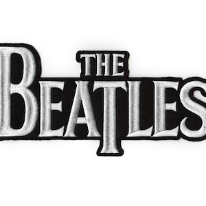 Puede incluir: Un parche bordado en blanco y negro con el texto "THE BEATLES" en una fuente de color plateado.