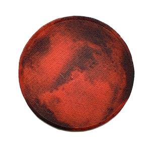 May include: A red and black round patch with a textured surface. The patch has a faded, distressed look.