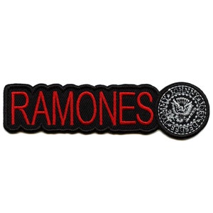 Könnte beinhalten: Schwarzer und roter gestickter Patch mit dem Wort "RAMONES" in roten Buchstaben und einem weißen und grauen gestickten Siegel mit den Worten "JOHNNY" und "PRESIDENT" oben und unten.
