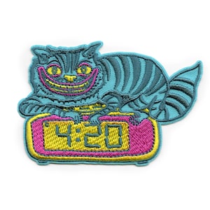 May include: Embroidered patch featuring a blue Cheshire Cat with a wide grin, sitting on a pink and yellow alarm clock displaying 4:20.