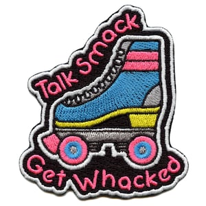 Op de afbeelding: Een geborduurde strijk-patch met een rolstoel en de tekst "Talk Smack Get Whacked". De rolstoel is blauw, geel en grijs met roze wielen. De tekst is roze en wit.