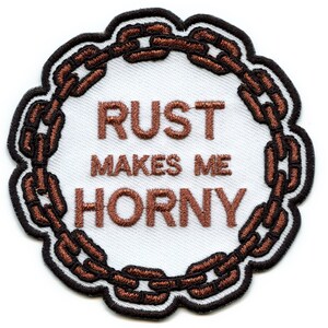 Puede incluir: Un parche bordado blanco con un borde de cadena marrón. El texto "RUST MAKES ME HORNY" está bordado en marrón.