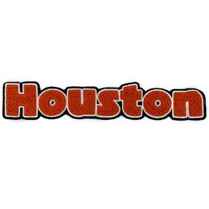 Puede incluir: Un parche de fieltro marrón con la palabra "Houston" en letras blancas con borde negro.