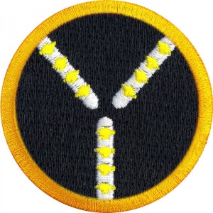 Op de afbeelding: Een geborduurde zwarte en gele patch met een gestileerd ritsontwerp. De rits is wit omrand en heeft gele tanden.