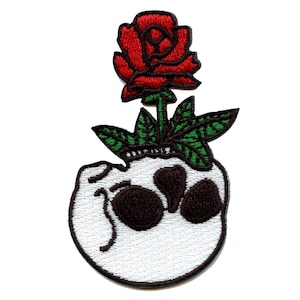 May include: Embroidered iron-on patch featuring a white skull with a red rose growing out of the top. The rose has green leaves and a brown stem.
