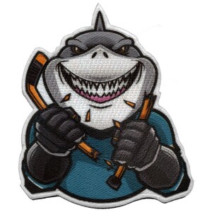 May include: A cartoon shark wearing a blue hockey jersey and holding two broken hockey sticks. The shark has a toothy grin and is wearing black gloves.