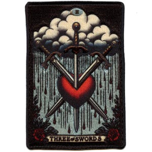 May include: A black and white embroidered patch featuring a heart pierced by three crossed swords. The heart is red, and the background is a blue sky with a white cloud and rain. The text "THREE of SWORDS" is at the bottom of the patch.