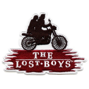 Puede incluir: Un parche bordado en rojo y blanco con la silueta de dos personas montando una motocicleta con el texto "THE LOST BOYS™" debajo.