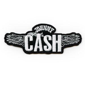Könnte beinhalten: Gestickter Aufnäher mit dem Namen "CASH" in Weiß und "JOHNNY" darüber. Der Aufnäher hat einen schwarzen Rand mit flügelartigen Designs, die eine Vintage-Ästhetik erzeugen. Ideal für Jacken, Taschen oder andere Kleidungsstücke.