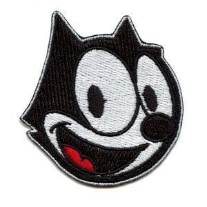 May include: Black and white embroidered patch of a cartoon cat with a large, toothy grin. The cat has a black nose and large, white eyes.