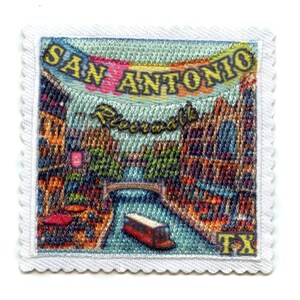 以下が含まれることがあります： サンアントニオ・リバーウォークのカラフルな画像が刺繍されたパッチ。水の上のボートと川沿いの建物が描かれています。パッチには「SAN ANTONIO Riverwalk TX」の文字が刺繍されています。