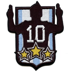 May include: Embroidered patch featuring a silhouette of a soccer player wearing a jersey with the number 10, against a blue and white striped background. Three gold stars are below the player.