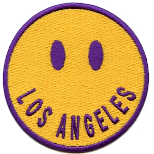 Könnte beinhalten: Gelber Smiley-Patch mit violetter Umrandung und dem Text "LOS ANGELES" in Violett.