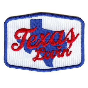 Può includere: Una toppa bianca con un contorno blu a forma di rettangolo con angoli arrotondati. La toppa presenta un contorno blu dello stato del Texas con il testo "Texas Lovin'" in lettere rosse corsive.