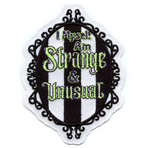May include: Embroidered patch with the text "I Myself Am Strange & Unusual" in green and purple. The patch has a black and white striped oval center, a decorative black border, and a white scalloped edge.