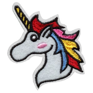 Puede incluir: Una aplicación de unicornio de fieltro blanco con una crin y un cuerno arcoíris. El unicornio tiene un contorno negro y un rubor rosa en la mejilla.